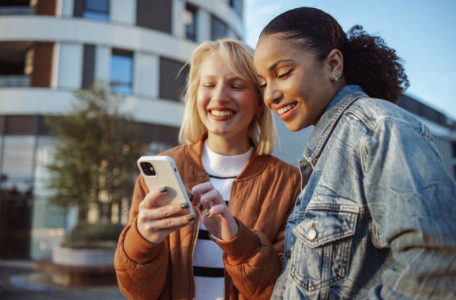 Two smiling friends looking at a phone, one holding it ready to pay